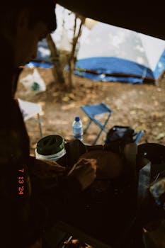 A person cooking at a campsite with tents and chairs, during daytime outdoors.