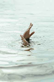 Close-up of hands reaching out of water with ripples and gentle movement, symbolizing help or struggle.