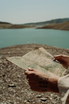 Hands holding a map by a tranquil lake, symbolizing exploration and adventure.