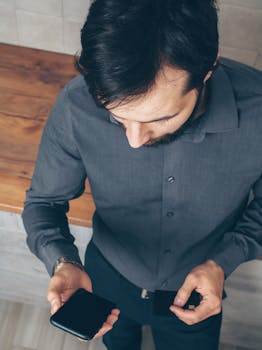 Top-down view of an adult man holding a smartphone and credit card, suggesting online shopping or financial transaction.