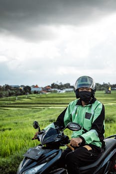 Motorbike rider wearing protective gear travels through scenic fields under an overcast sky.